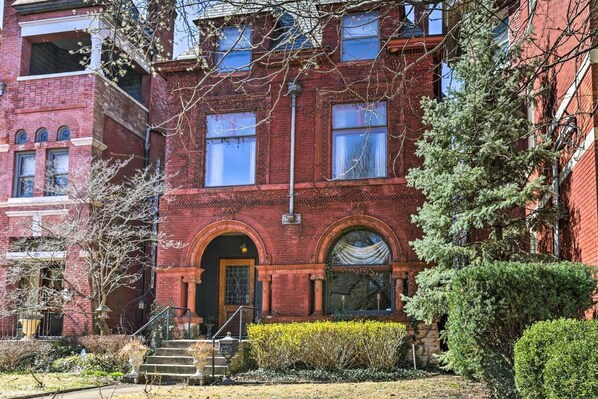 A red brick building with two-story windows, a front entrance with a door, and a small set of steps leading up to the entrance.