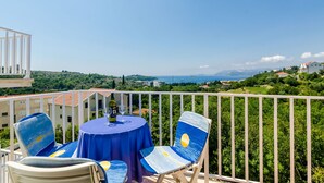 A balcony with a table and chairs, overlooking a scenic landscape with greenery and buildings. - Apartment Alba (Konavle)