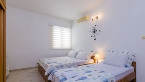 A bedroom with two beds, a window with blinds, a wall-mounted air conditioner, and a wall decoration. - Apartment Alba (Konavle)