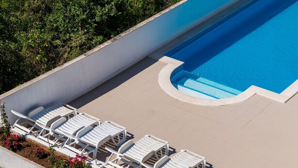 A swimming pool with white lounge chairs and a flower bed. - Apartment Alba (Konavle)