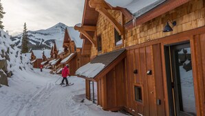 A wooden cabin with a ski slope leading to it, surrounded by snow-covered mountains.