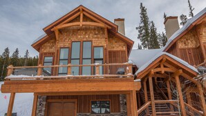 A wooden cabin with a balcony, stone foundation, and a chimney.