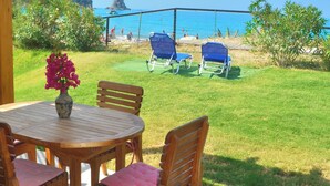 Eine überdachte Terrasse mit Holztisch und -stühlen, einem Blumenstrauß und Blick auf Strand und Meer.