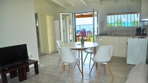 Ein modernes Wohnzimmer mit Flachbildfernseher, einem Essbereich mit Tisch und Stühlen sowie einer Küche mit Blick aus dem Fenster.