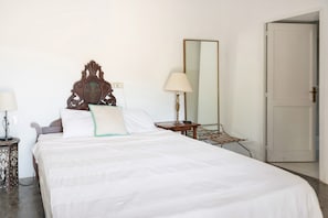 Een net opgemaakt bed met witte lakens, een houten hoofdbord met decoratief ontwerp, een bedlampje en een spiegel aan de muur.