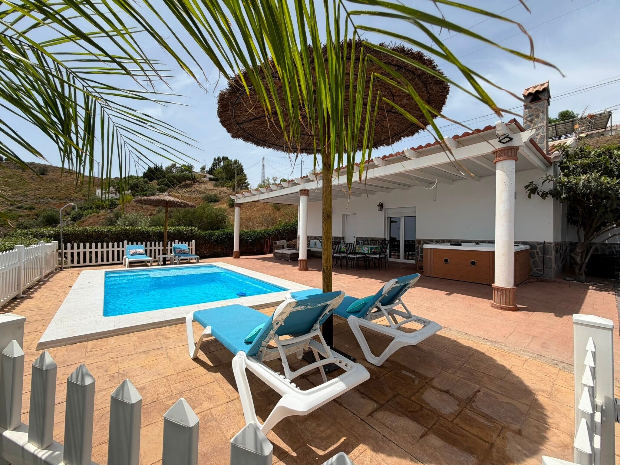 Una piscina con sillones de descanso, un porche techado y vistas al paisaje circundante.