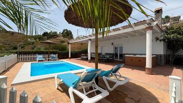 Una piscina con sillones de descanso, un porche techado y vistas al paisaje circundante.