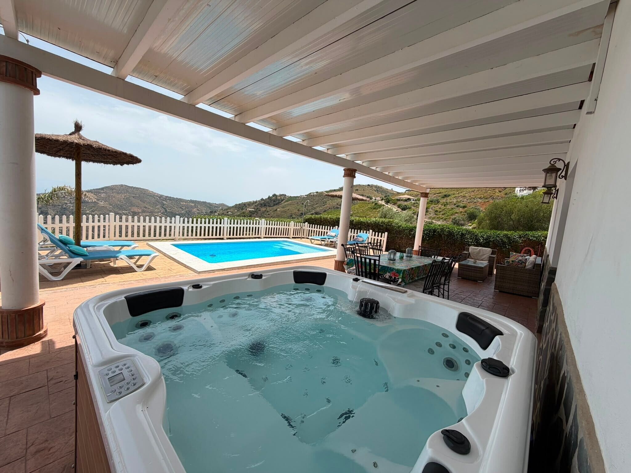 Un jacuzzi con piscina y sillas de descanso, rodeado por una pérgola blanca y una valla blanca.