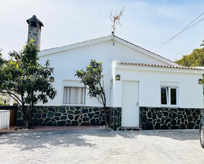 A white building with a stone base, a chimney, and a car parked in front. - “Casa Rural el Cerrillo” Mountain View, Wi-Fi, Garden, Terrace & Pool (Cómpeta)