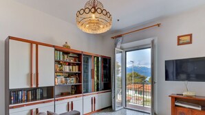 A living room with a large sofa, a bookshelf, a TV, and a view of mountains through a glass door. - Nice apartment for 6 people with WIFI, TV, terrace and pets allowed (Portoferraio)