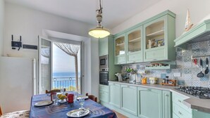 A kitchen with light green cabinets, a dining table set with plates and glasses, and a view of the sea through a window. - Nice apartment for 6 people with WIFI, TV, terrace and pets allowed (Portoferraio)