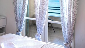 A bedroom with a bed, a window with curtains, and a view of the sea.