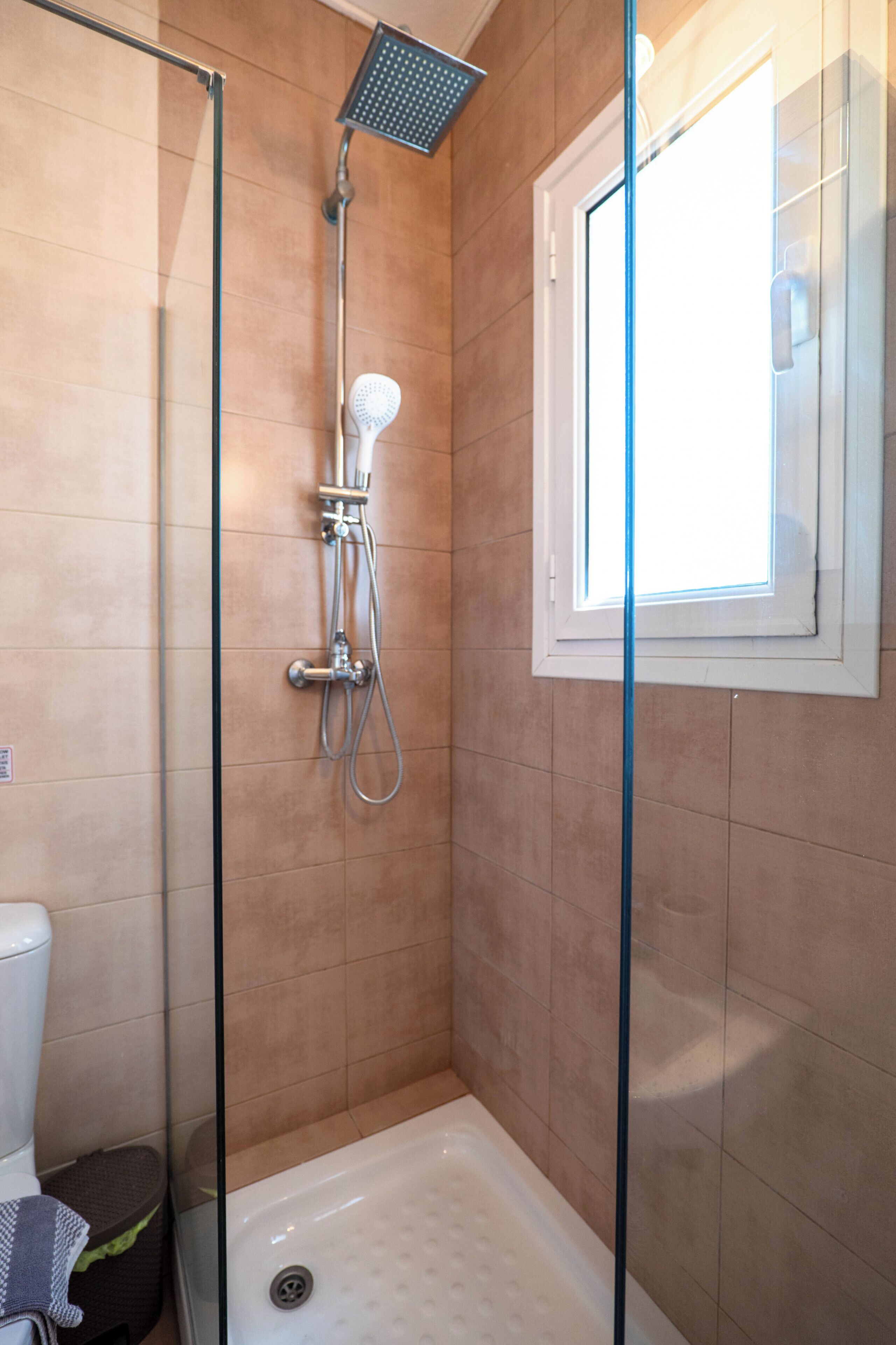 A shower with a glass door, a window, and a bathtub.