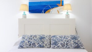 Una cama con almohadones estampados, cabecera y dos lámparas fijadas a la pared.