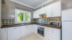 Una cocina con armarios blancos, lavavajillas, horno, microondas y ventana con vista a zonas verdes.