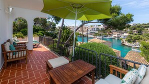 Una terraza con sombrilla verde, mobiliario de madera y vistas a un puerto deportivo y edificios.
