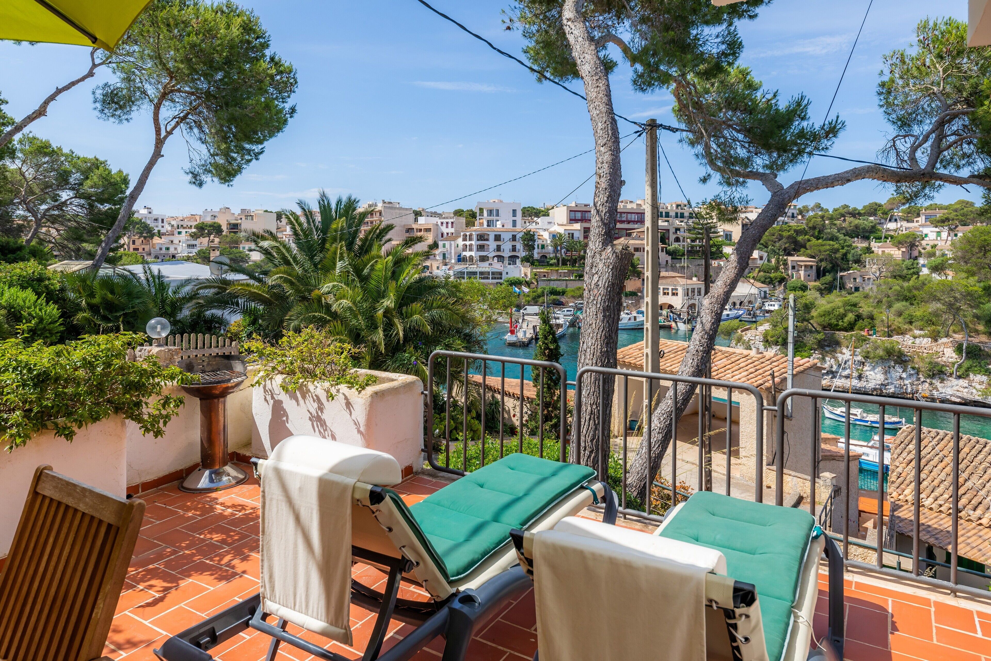 Een balkon met twee loungestoelen, een barbecue en uitzicht op een kustplaatsje.