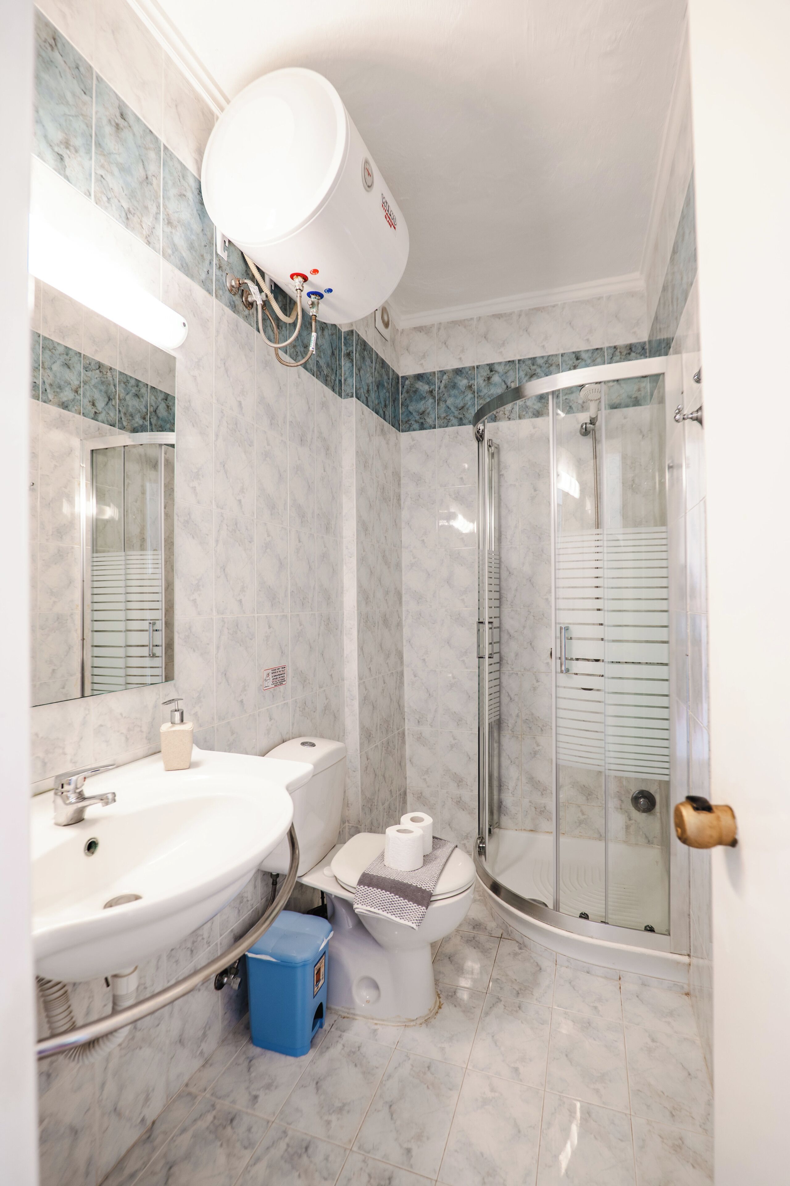 A bathroom with a shower, sink, toilet, and a large mirror.