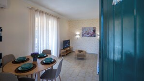 A dining area with a table set for four, a television on a stand, and a painting on the wall. - Corfu Glyfada Menigos Resort 46 (Corfu)