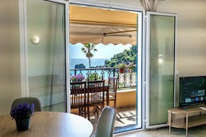 A room with a balcony, a dining table, chairs, a TV, and a potted plant. - Corfu Glyfada Menigos Resort 46 (Corfu)
