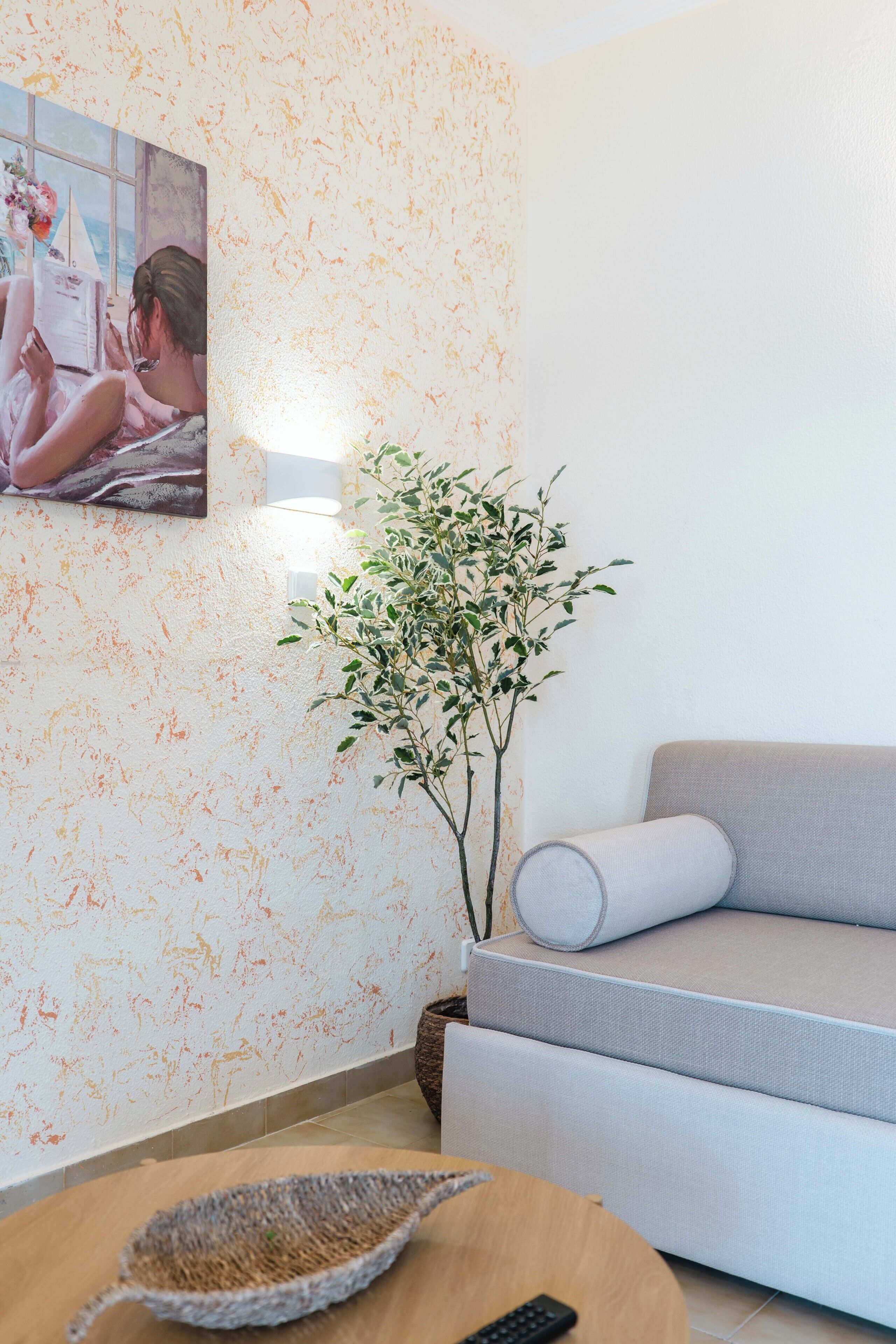 Uma sala de estar com um sofá, um quadro, uma planta e uma cesta de vime sobre uma mesa.