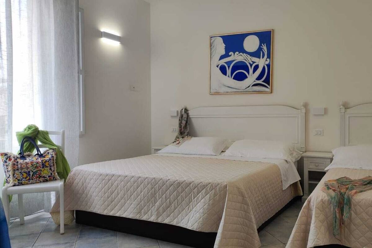 Un dormitorio con dos camas, una mesita de noche, una silla y un cuadro en la pared.