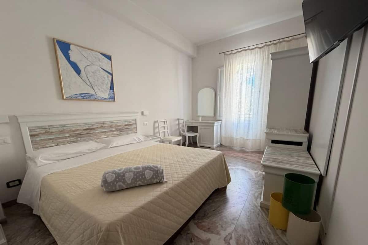 Una habitación de hotel con cama, escritorio, silla, televisión y un cuadro en la pared.