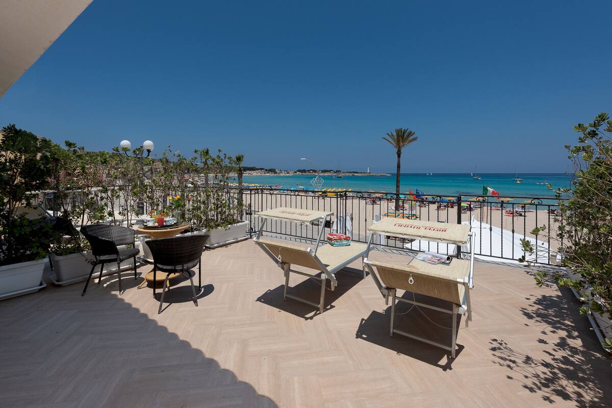 Un balcón con mobiliario exterior, vista a la playa y cielo azul despejado.