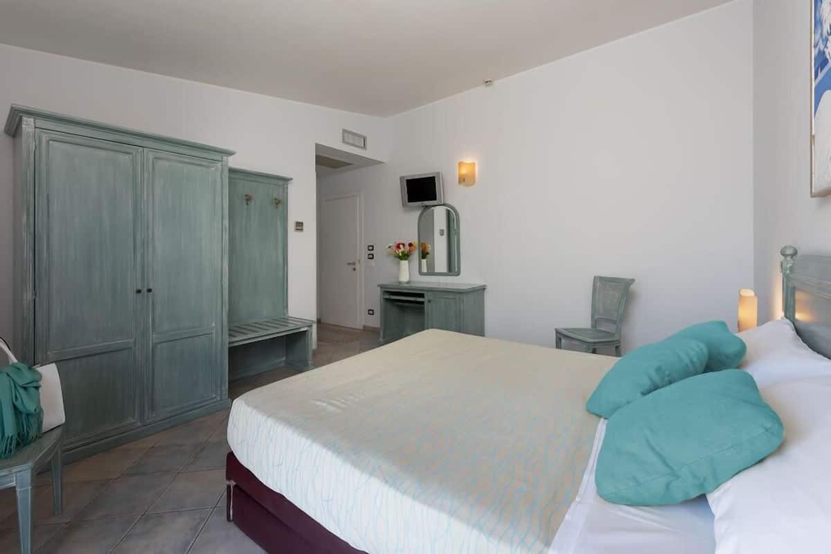 Un dormitorio con cama, armario, televisor, espejo y una silla.