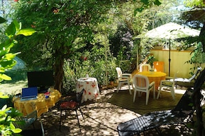 Une terrasse avec un ordinateur portable posé sur une table, entourée de chaises et d’une autre table recouverte d’une nappe jaune.