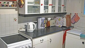 Een keuken met witte kastjes, een fornuis, een koffiezetapparaat en diverse keukengerei.