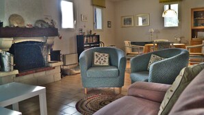 Een woonkamer met een open haard, twee fauteuils, een bank en een boekenkast.