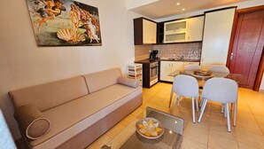Un espacio habitable compacto con sofá, mesa de comedor, sillas, máquina de café y un cuadro en la pared.