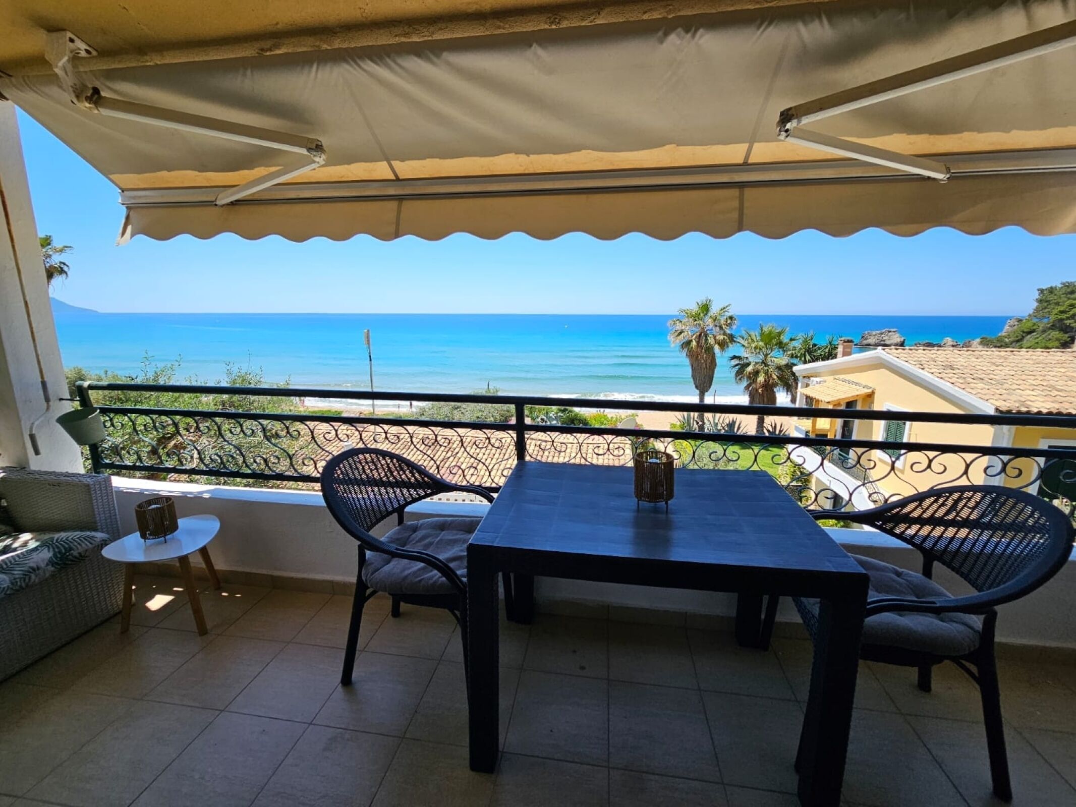Ein Balkon mit Tisch und Stühlen mit Blick auf einen Strand und das Meer.