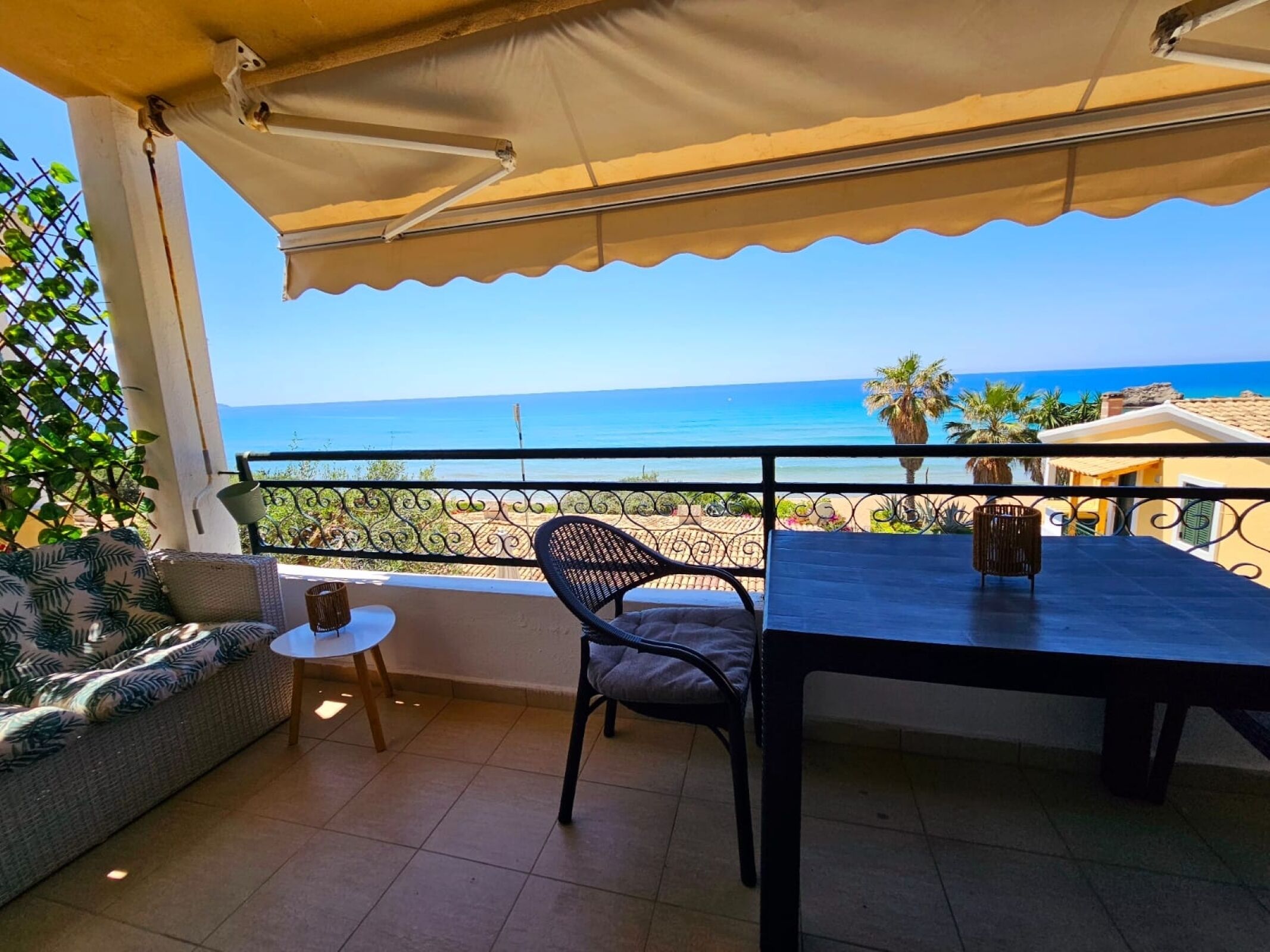 A balcony with a view of the sea, a table, a chair, and a sofa.