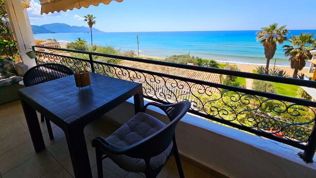 Un balcón con mesa y sillas, con vista a una playa y el mar.