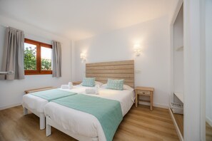 A double bed with a wooden headboard, two bedside tables, a window with curtains, and a view of greenery outside.