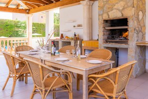 An outdoor dining area with wicker chairs and a stone fireplace. - Apartment Close to the Beach with Pool Access, Private Terrace, Air Conditioning and Wi-Fi (Canyamel)