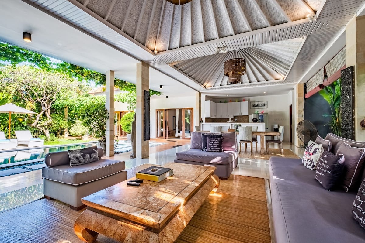 Amplia sala de estar con piscina, muebles modernos y una cocina al fondo.