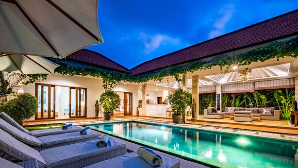 A poolside area with lounge chairs, a pool, and a covered seating area with a sofa and cushions.