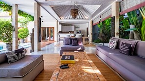 A modern living room with a sofa, a coffee table, and a view of the kitchen and pool area.