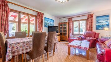 A living room with a dining table, chairs, a sofa, a TV, and a cabinet.