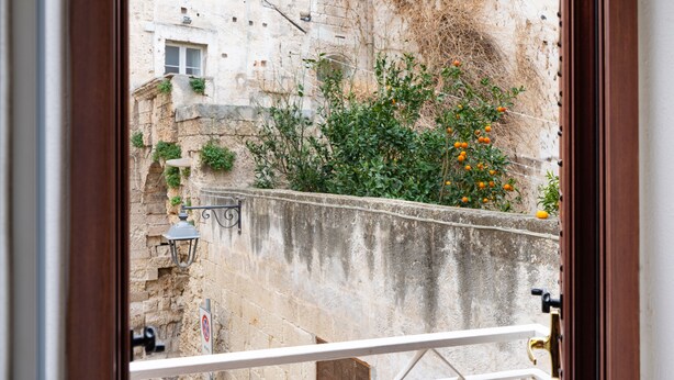 A view from a balcony with a stone wall, a small tree with orange fruits, and a building with windows and a door. - Vico Delle Palme (Monopoli)
