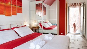 A hotel room with a large bed, red accents, a glass-enclosed bathroom, and a view of the outdoors. - Vico Delle Palme (Monopoli)