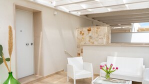 A room with white wicker furniture, a glass coffee table, and a door with a towel rack. - Suite Martino Seaview (Monopoli)