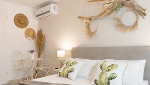 A bedroom with a bed, two chairs, a small table, and decorative wall art including a cactus pillow and a woven wall hanging. - Suite Martino Seaview (Monopoli)