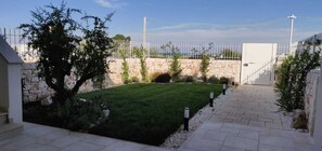 Un jardín con muro de piedra, césped y un camino pavimentado.