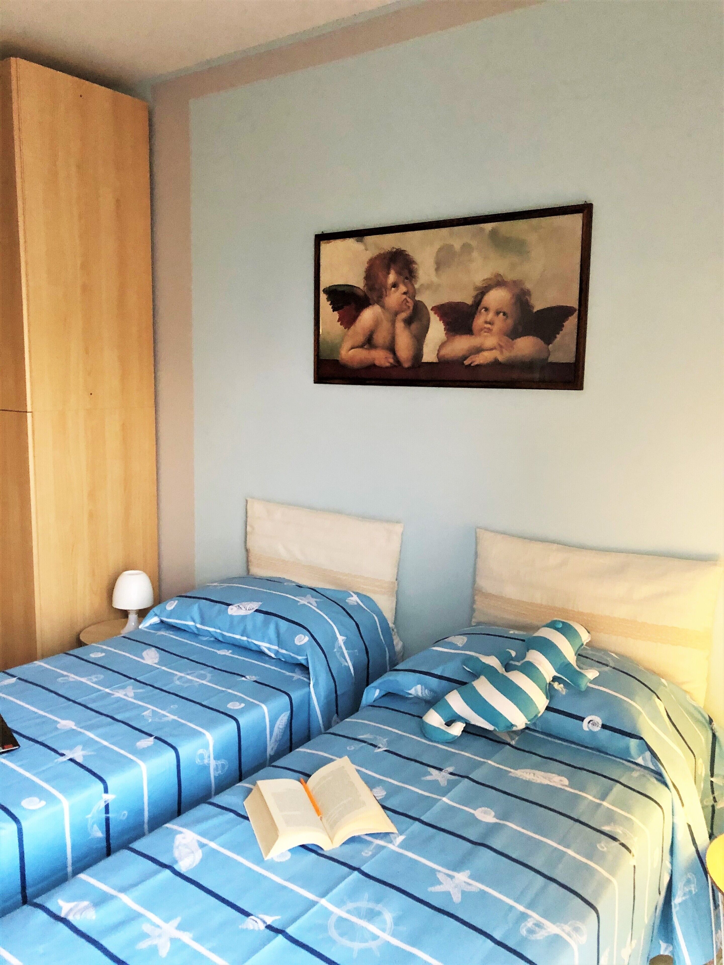 A bedroom with two beds, a wooden wardrobe, and a painting on the wall.