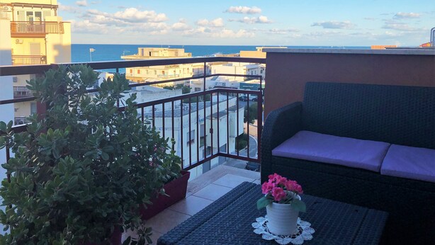 A balcony with a view of the sea, a potted plant, and a cushioned seating area. - Stella del Mare (Monopoli)