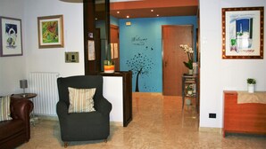 A living room with a black armchair, a brown sofa, a small table with a lamp, and a blue wall with a welcome sign. - Stella del Mare (Monopoli)